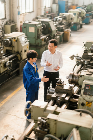 工厂车间师傅指导年轻工人操作机器